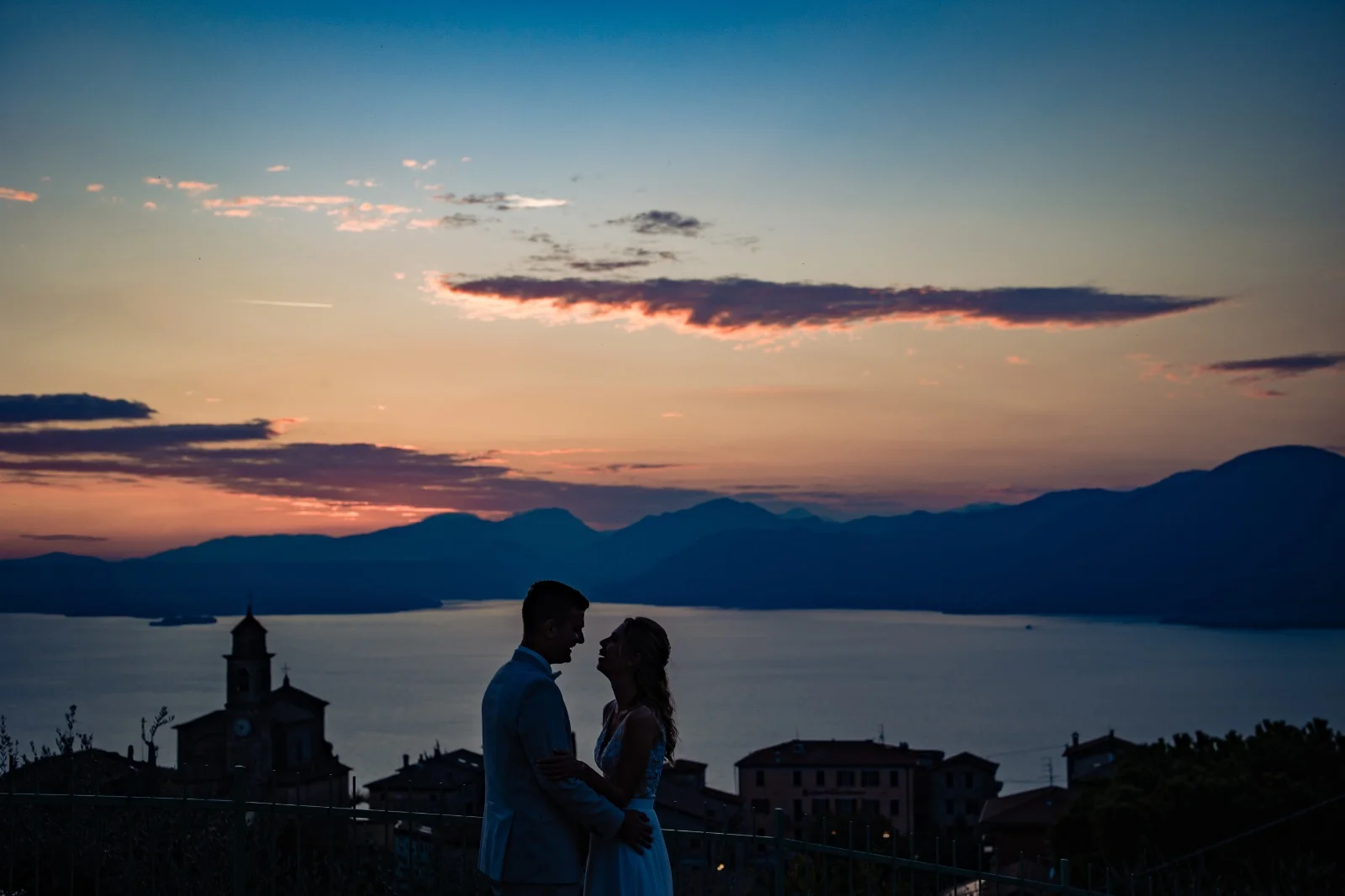 Sposi al tramonto sul Lago di Garda Sposi in controluce al tramonto sul Lago di Garda con il campanile di Albisano
